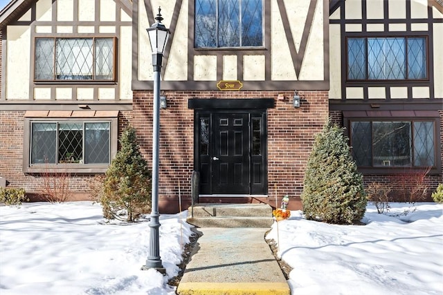 snow covered property entrance with stucco siding and brick siding