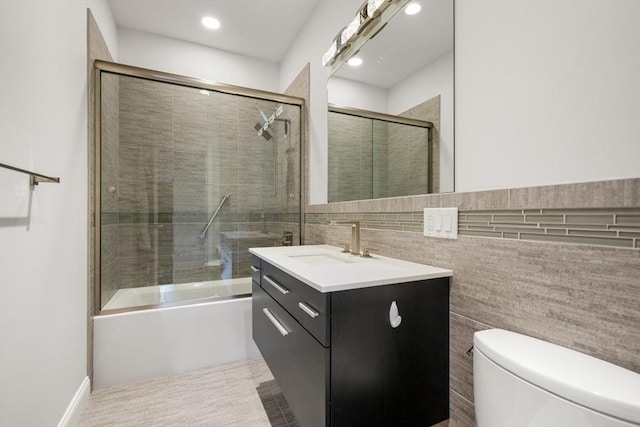 bathroom featuring toilet, tile walls, vanity, enclosed tub / shower combo, and recessed lighting