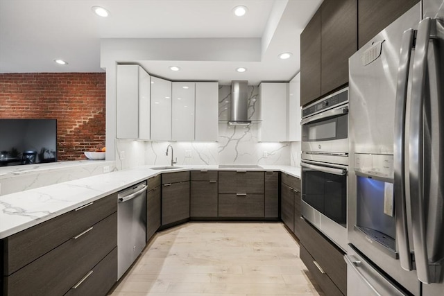 kitchen with appliances with stainless steel finishes, wall chimney range hood, modern cabinets, a sink, and white cabinets