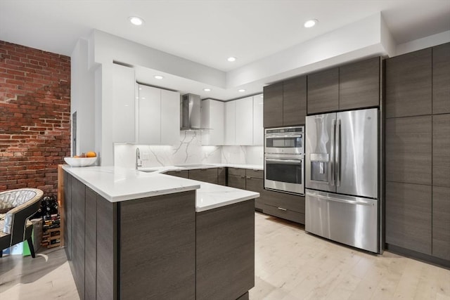kitchen with stainless steel appliances, wall chimney exhaust hood, modern cabinets, a peninsula, and brick wall