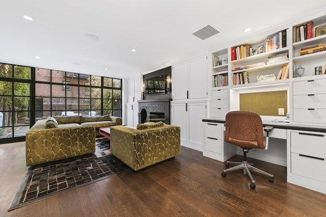 home office featuring a fireplace, visible vents, built in study area, floor to ceiling windows, and dark wood finished floors