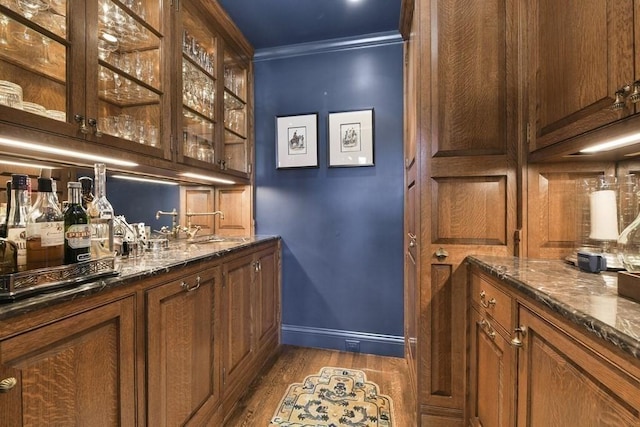 bar featuring dark wood finished floors, ornamental molding, a sink, bar, and baseboards