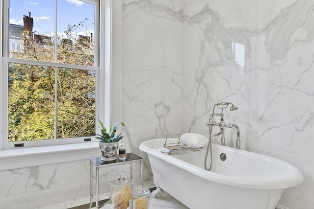 bathroom featuring plenty of natural light, marble finish floor, a soaking tub, and stone wall