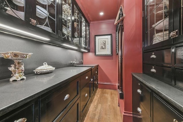 bar with light wood-type flooring, baseboards, crown molding, and a sink