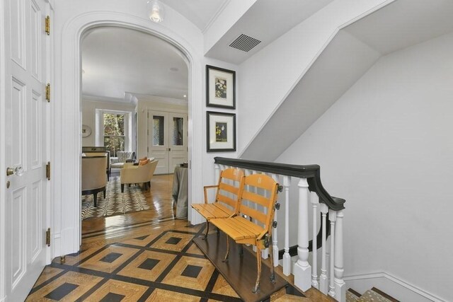 hallway featuring arched walkways, crown molding, visible vents, baseboards, and stairs