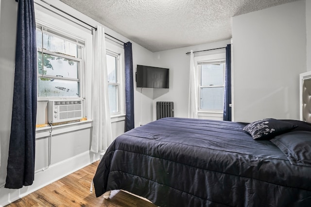 bedroom with radiator, a textured ceiling, multiple windows, and hardwood / wood-style flooring