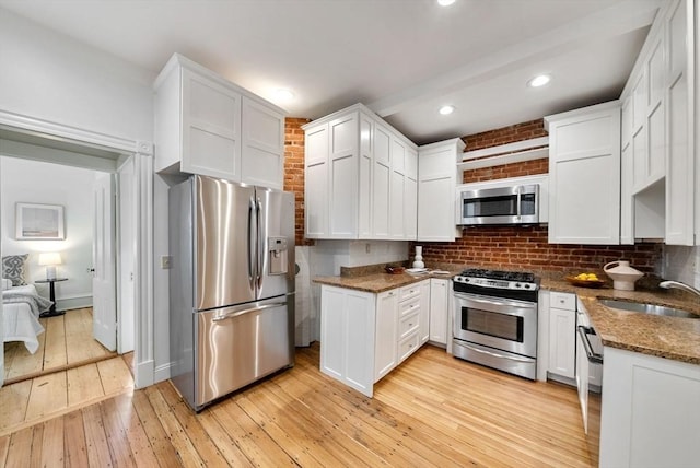 kitchen featuring stainless steel appliances, white cabinets, a sink, and light wood-style flooring