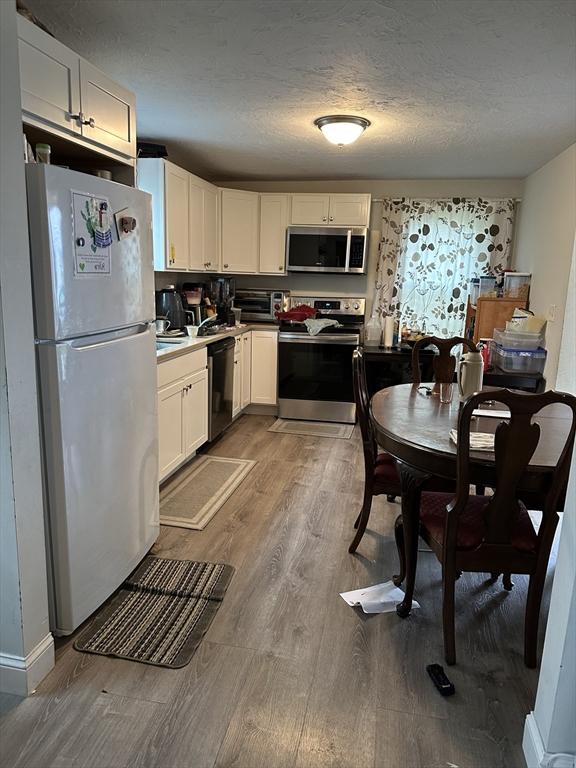 21 Sigel St, Worcester, MA 01610 - kitchen featuring stainless steel appliances, wood finished floors, white cabinetry, a textured ceiling, and baseboards
