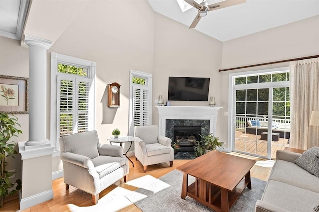 living room with decorative columns, light wood-type flooring, a premium fireplace, baseboards, and a high ceiling