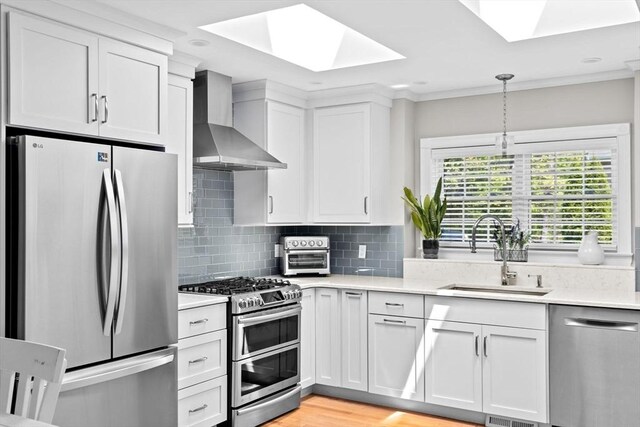 kitchen with stainless steel appliances, a skylight, a sink, wall chimney range hood, and crown molding