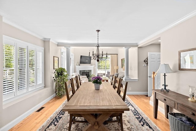 dining space featuring decorative columns, crown molding, light wood-style flooring, baseboards, and a fireplace