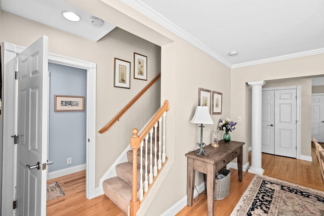 foyer featuring ornate columns, light wood-style flooring, ornamental molding, baseboards, and stairway