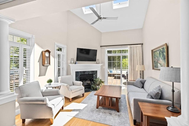 living area featuring a skylight, high vaulted ceiling, wood finished floors, a high end fireplace, and a ceiling fan