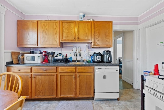 kitchen with dark countertops, ornamental molding, brown cabinetry, a sink, and white appliances