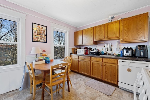 kitchen featuring white appliances, brown cabinetry, dark countertops, and a sink