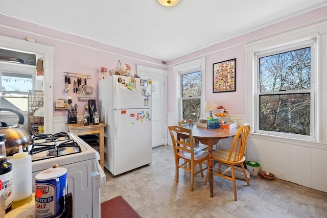 kitchen featuring a wealth of natural light, white appliances, wainscoting, and crown molding