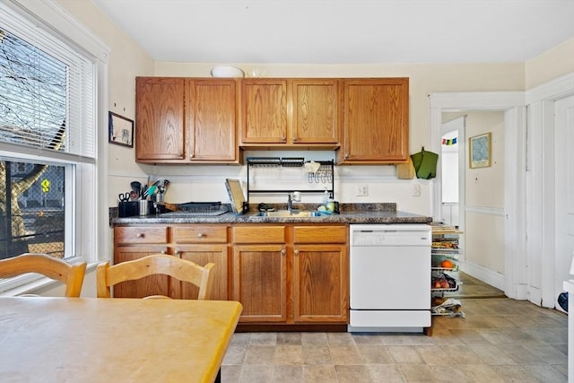 kitchen featuring dark countertops, brown cabinets, dishwasher, and a sink