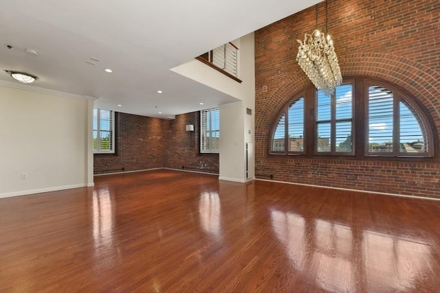 unfurnished living room with brick wall, a chandelier, baseboards, and wood finished floors