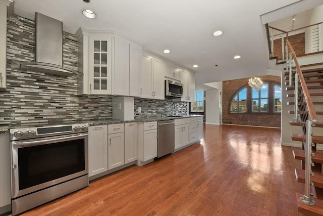 kitchen featuring appliances with stainless steel finishes, wall chimney range hood, a sink, light wood finished floors, and recessed lighting
