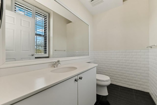 bathroom featuring tile walls, tile patterned floors, vanity, toilet, and a wainscoted wall
