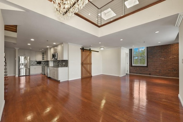 unfurnished living room with a barn door, baseboards, ornamental molding, dark wood-style floors, and a chandelier