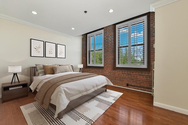 bedroom featuring baseboards, wood finished floors, recessed lighting, brick wall, and ornamental molding