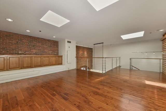 empty room with a skylight, wood-type flooring, brick wall, and recessed lighting