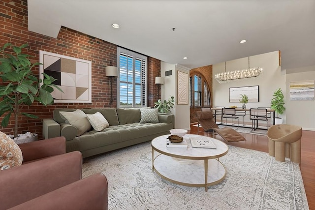 living area with brick wall, wood finished floors, recessed lighting, a chandelier, and baseboards