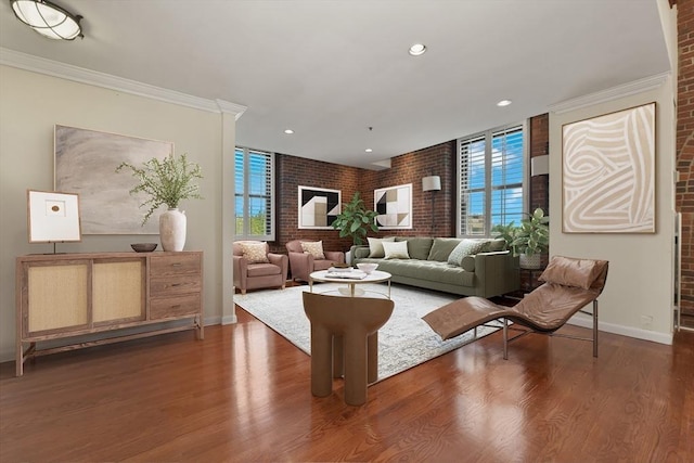 living room featuring brick wall, wood finished floors, baseboards, recessed lighting, and ornamental molding