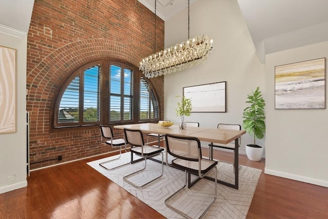 dining space featuring baseboards, a chandelier, wood finished floors, and high vaulted ceiling