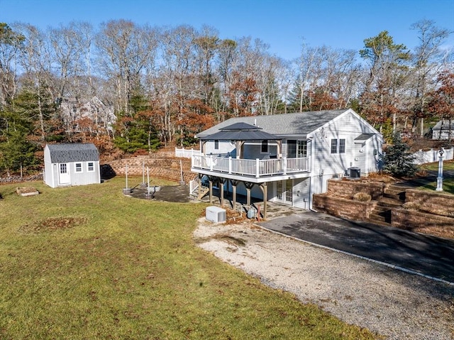 back of property with a wooden deck, a yard, and a storage unit