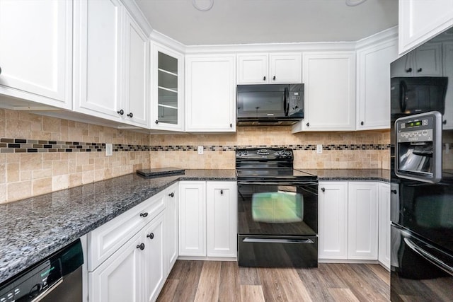 kitchen featuring white cabinets, light hardwood / wood-style floors, dark stone countertops, and black appliances