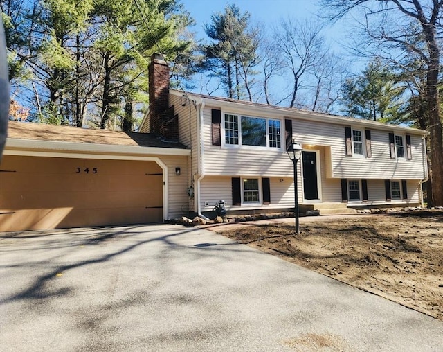 bi-level home featuring aphalt driveway, a garage, and a chimney