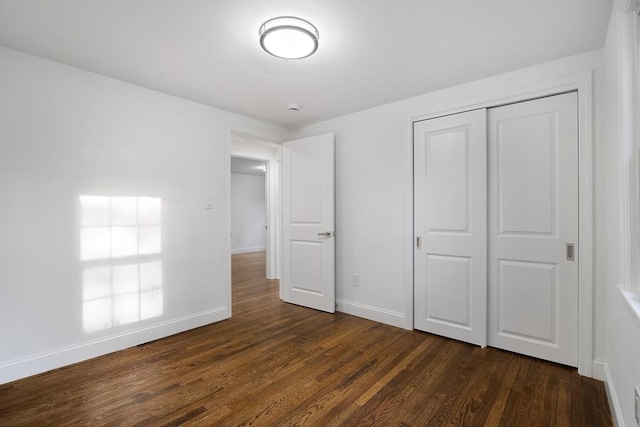 unfurnished bedroom with baseboards, dark wood-style flooring, and a closet