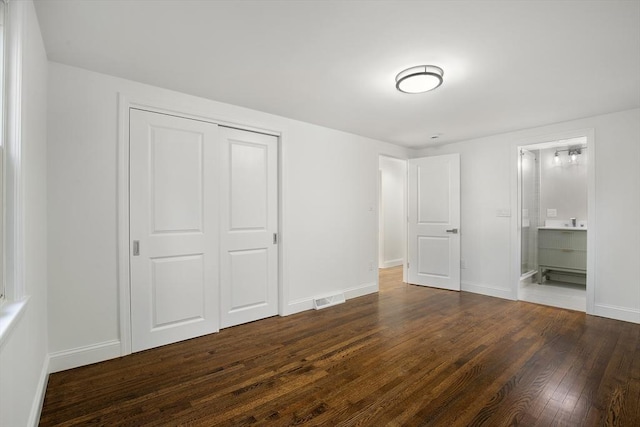 unfurnished bedroom featuring visible vents, baseboards, a closet, dark wood-style floors, and ensuite bath