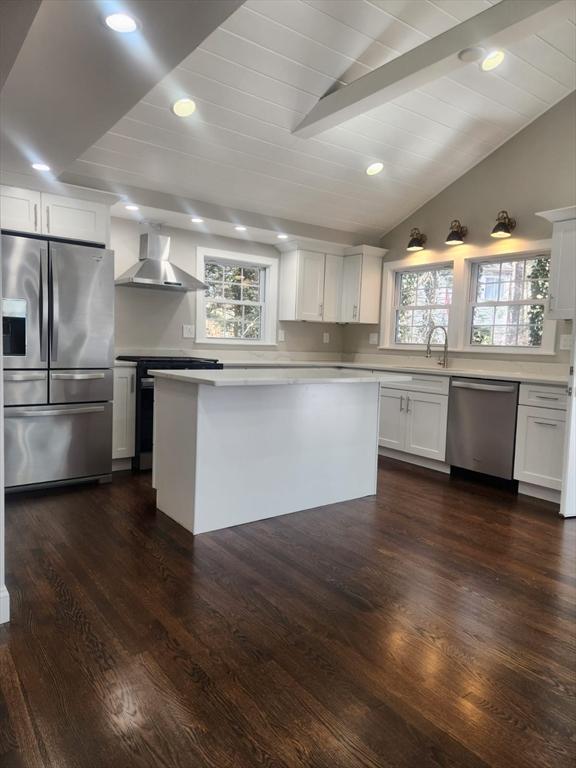 kitchen featuring plenty of natural light, lofted ceiling with beams, stainless steel appliances, and wall chimney exhaust hood