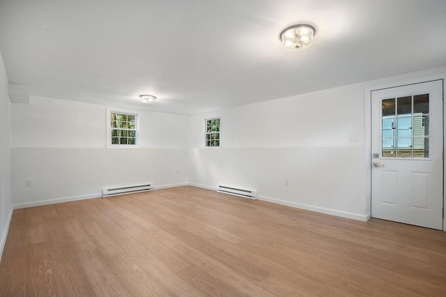 unfurnished room with a baseboard heating unit, baseboards, and light wood-type flooring