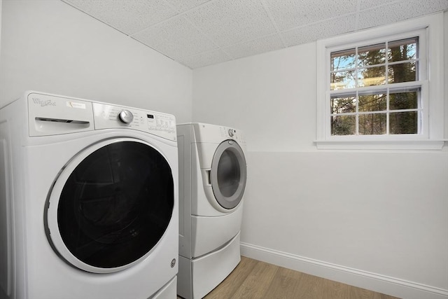 clothes washing area featuring laundry area, light wood-style flooring, washing machine and dryer, and baseboards