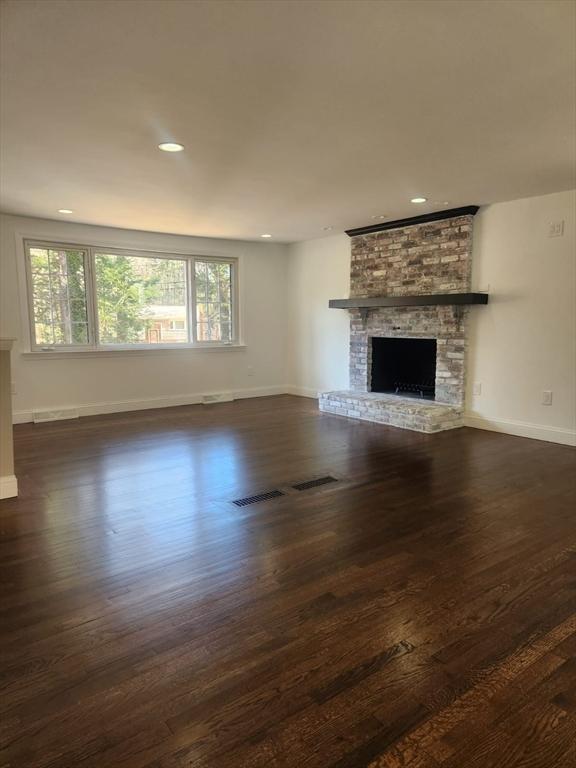 unfurnished living room with recessed lighting, baseboards, a brick fireplace, and dark wood-style floors