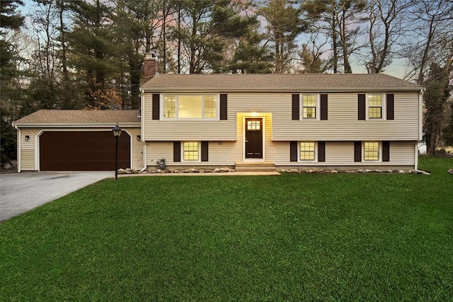 raised ranch featuring a front lawn, driveway, a chimney, and a garage