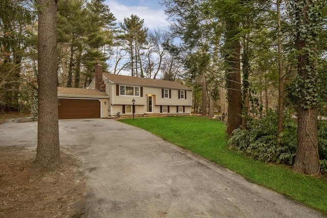 bi-level home featuring a front lawn, a garage, driveway, and a chimney