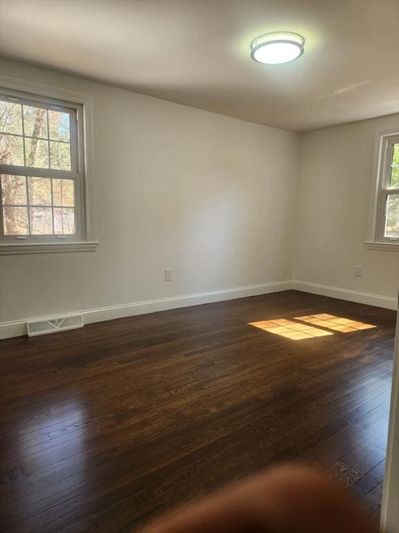 empty room with visible vents, baseboards, and dark wood-style floors