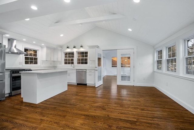 kitchen with appliances with stainless steel finishes, wall chimney exhaust hood, vaulted ceiling with beams, and light countertops