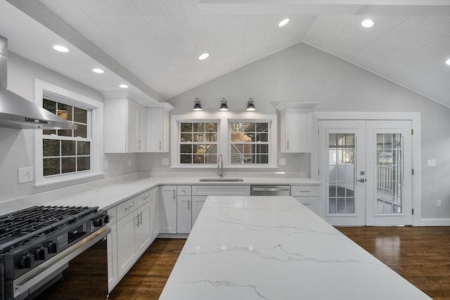 kitchen featuring a sink, wall chimney exhaust hood, gas range oven, and white cabinets