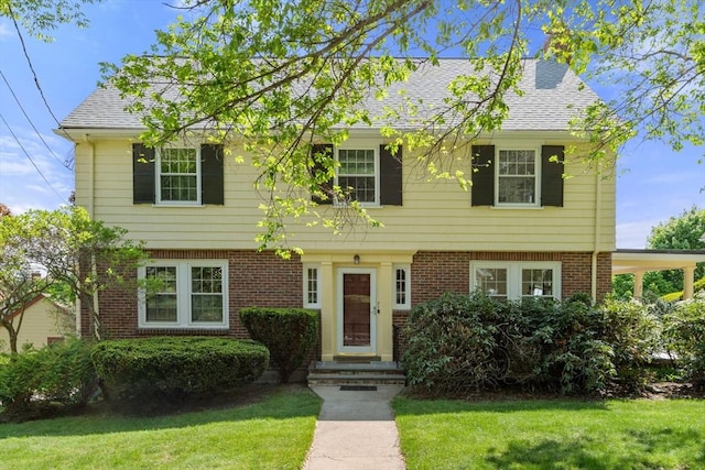 colonial inspired home with a front lawn, brick siding, and roof with shingles