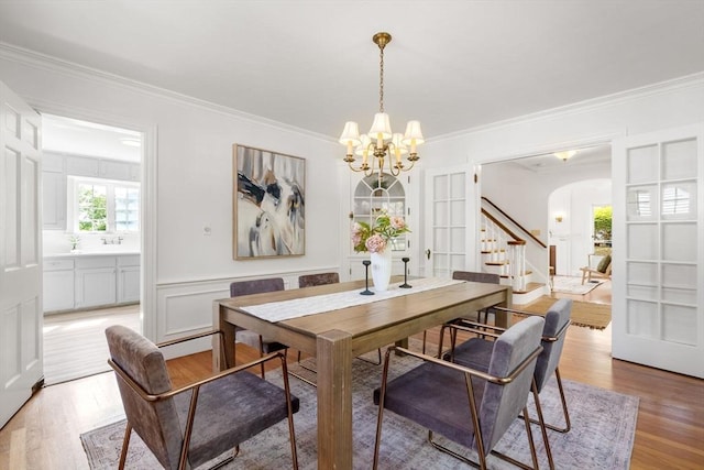 dining space featuring a chandelier, stairs, light wood finished floors, arched walkways, and crown molding
