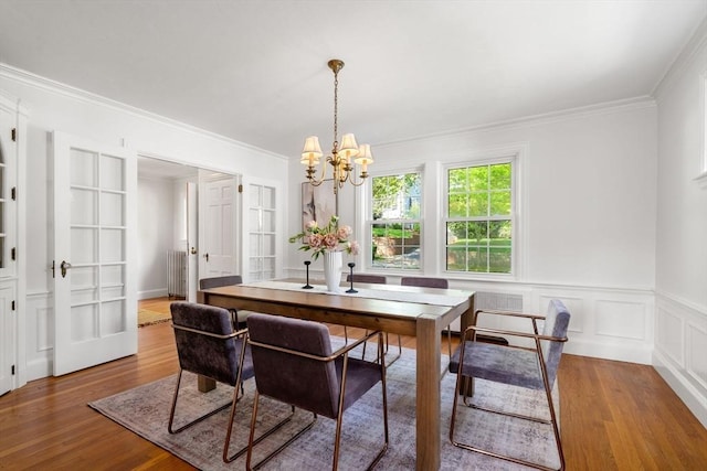 dining space featuring a chandelier, wood finished floors, crown molding, and wainscoting
