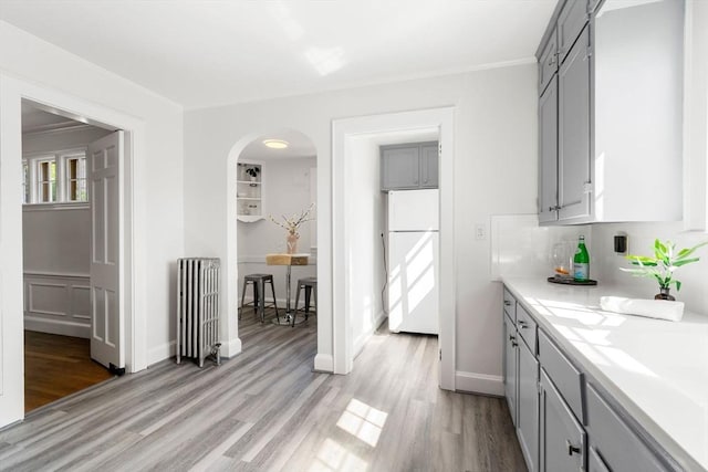kitchen featuring radiator, gray cabinetry, freestanding refrigerator, light wood-type flooring, and light countertops
