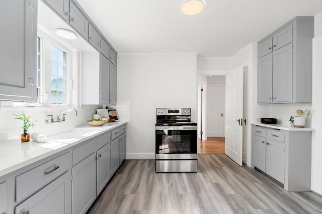 kitchen with stainless steel range with electric cooktop, gray cabinetry, light wood-style floors, and a sink