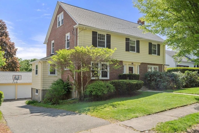 view of front facade with brick siding, a chimney, a front lawn, and a detached garage